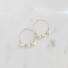 Two 30mm hoop Arianna earrings with gold plating and three freshwater pearls on each earring placed side by side on a marble surface