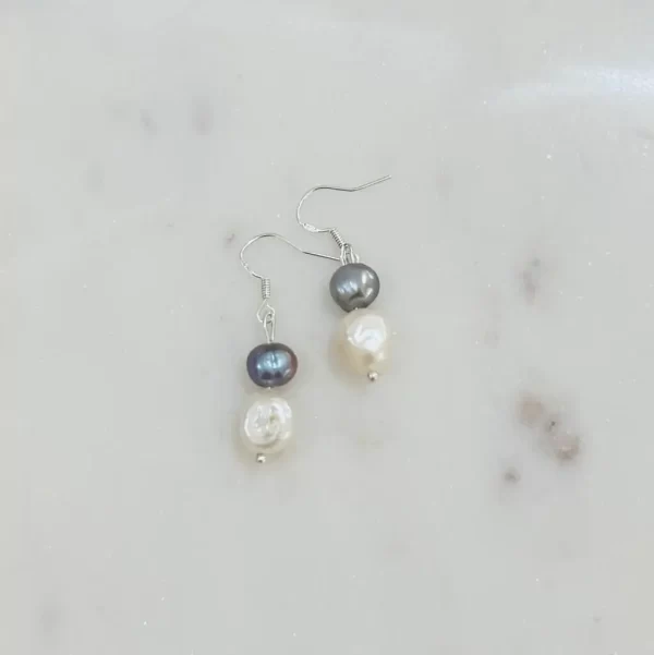 Two silver hook earrings with silver plating holding a something blue pearl and ivory pearl on each earring placed side by side on a marble surface